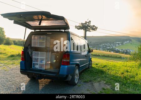 Vanlife. Pulmino blu parcheggiato di fronte a una splendida vista a Willingen Upland, in Germania. Accanto al veicolo c'è uno skilift. Il bagagliaio è aperto. Piatti fatti in casa Foto Stock