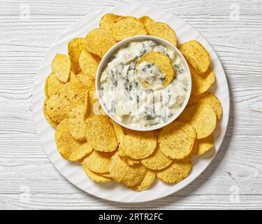 salsa cremosa di spinaci di carciofi e mandorle con patatine fritte su piatto bianco su un tavolo di legno bianco, vista orizzontale dall'alto, vista ravvicinata, piatto Foto Stock