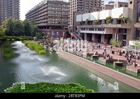 Persone che si rilassano sulla terrazza sul lago vicino alle fontane d'acqua in estate all'esterno dell'edificio artistico del Barbican Centre a Londra, Inghilterra, KATHY DEWITT Foto Stock