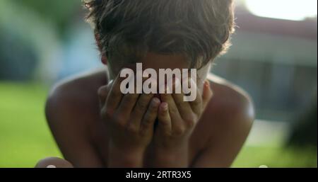 Bambino che copre la faccia con vergogna. Ragazzo che ostacola la faccia con le mani Foto Stock