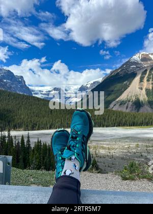 Le persone con i piedi in alto ammirano la vista panoramica del fiume Athabasca e delle montagne circostanti nel Jasper National Park, in Canada, in una splendida posizione Foto Stock