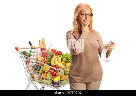 Donna pensiva con un carrello che guarda una banconota isolata su sfondo bianco Foto Stock