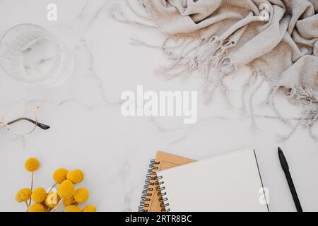 Quaderno bianco con spazio per la copia di testo, occhiali e fiori gialli su sfondo di marmo bianco. Vista dall'alto. Scrivania da ufficio con ingombro minimo. Lavoro o Foto Stock