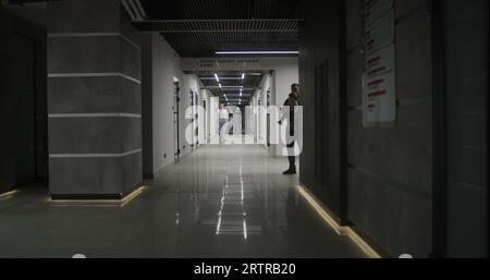 Medici, operatori sanitari e pazienti camminano lungo il luminoso corridoio della clinica. Personale medico e persone in ospedale privato o moderno centro medico. Laboratorio o stazione di emergenza. Vista posteriore. Foto Stock