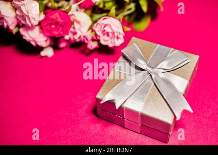 Confezione regalo argento con fiocco e rose di seta isolate sul rosa Foto Stock