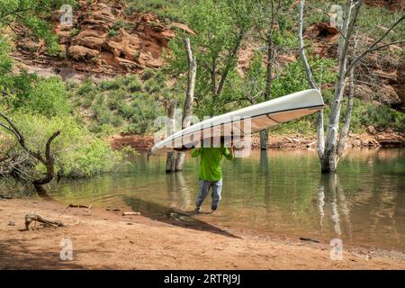 Il maschio anziano sta portando una canoa di spedizione decked ai piedi delle colline del Colorado del nord in paesaggio primaverile Foto Stock