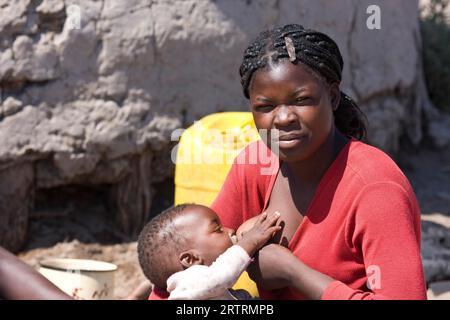 Donna africana che allatta il suo bambino, seduta davanti alla capanna di fango, Botswana Foto Stock