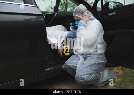 Criminologo che scatta foto di prove sulla scena del crimine con un cadavere in macchina Foto Stock