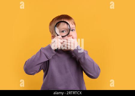 Un ragazzo sorpreso che guardasse attraverso la lente di ingrandimento su sfondo giallo Foto Stock