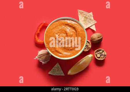 Ciotola di gustoso muhammara e ingredienti su sfondo rosso Foto Stock