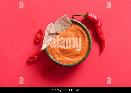 Ciotola di gustosi muhammara e peperoncino su sfondo rosso Foto Stock