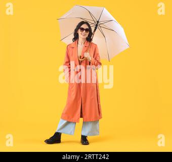 Elegante giovane donna asiatica in abiti autunnali con ombrello su sfondo giallo Foto Stock