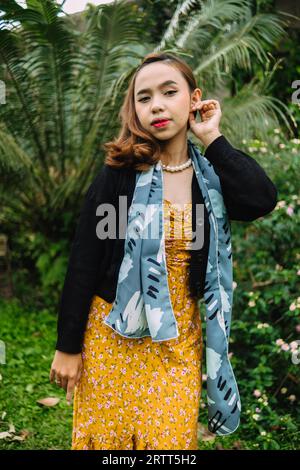 una donna glamour con collana di perle e abito giallo si sta godendo un giardino pieno di fiori nel pomeriggio Foto Stock