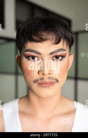 Un uomo asiatico che indossa una camicia bianca con maniche aperte e trucco sul viso di notte Foto Stock