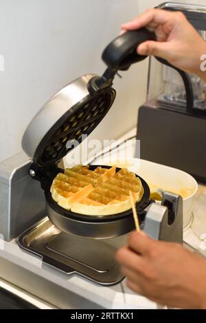 il cuoco controlla l'impasto per i waffle dolci nel ferro da stiro con un bastoncino di legno Foto Stock