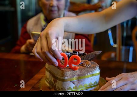 Mani di un giovane che mette candele sulla torta, celebrando il 90° compleanno della nonna. Foto Stock