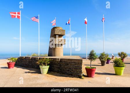 Monumento segnaletico a Bernières-sur-Mer, Francia, eretto nel 1950 sul sito dello sbarco in Normandia della seconda guerra mondiale di Juno Beach, circondato dalle bandiere degli Alleati. Foto Stock