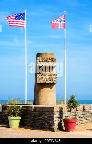 Monumento segnaletico a Bernières-sur-Mer, Francia, eretto nel 1950 sul sito dello sbarco in Normandia della seconda guerra mondiale di Juno Beach, circondato dalle bandiere degli Alleati. Foto Stock