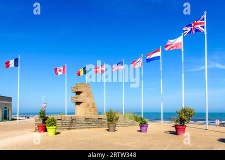 Monumento segnaletico a Bernières-sur-Mer, Francia, eretto nel 1950 sul sito dello sbarco in Normandia della seconda guerra mondiale di Juno Beach, circondato dalle bandiere degli Alleati. Foto Stock