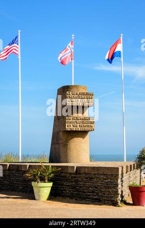 Monumento segnaletico a Bernières-sur-Mer, Francia, eretto nel 1950 sul sito dello sbarco in Normandia della seconda guerra mondiale di Juno Beach, circondato dalle bandiere degli Alleati. Foto Stock