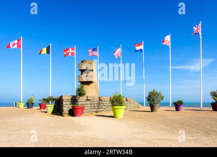 Monumento segnaletico a Bernières-sur-Mer, Francia, eretto nel 1950 sul sito dello sbarco in Normandia della seconda guerra mondiale di Juno Beach, circondato dalle bandiere degli Alleati. Foto Stock