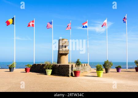 Monumento segnaletico a Bernières-sur-Mer, Francia, eretto nel 1950 sul sito dello sbarco in Normandia della seconda guerra mondiale di Juno Beach, circondato dalle bandiere degli Alleati. Foto Stock