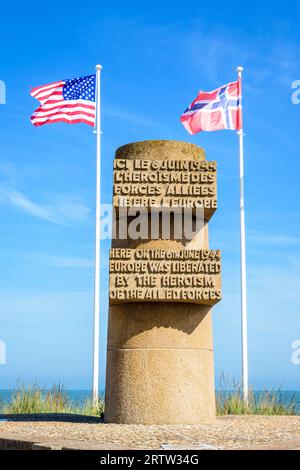 Monumento segnaletico a Bernières-sur-Mer, Francia, eretto nel 1950 sul sito dello sbarco in Normandia della seconda guerra mondiale di Juno Beach, circondato dalle bandiere degli Alleati. Foto Stock