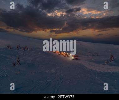 Gli snowboarder (motoslitte per gatti delle nevi) durante l'escursione notturna prima dell'alba fanno un giro in cima alla montagna invernale con freerider e snowboarder. Stazione sciistica alpina di Dragob Foto Stock