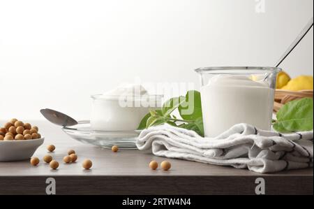 Yogurt di soia su tavola di legno con fagioli di soia secchi e foglie con sfondo bianco isolato. Vista frontale. Foto Stock