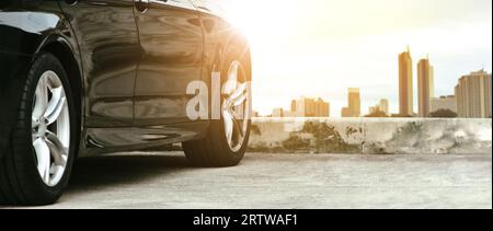 Primo piano di un'auto nera sullo sfondo del paesaggio urbano con la luce del sole, parcheggio auto nel parcheggio, banner panoramico, concetto di trasporto Foto Stock