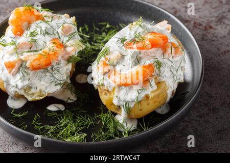 Patate al forno ripiene di salsa di panna acida, aglio, aneto e gamberi da vicino in un piatto sul tavolo. Orizzontale Foto Stock