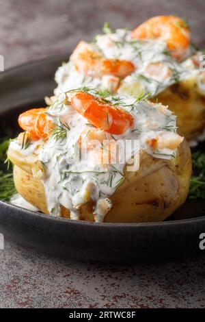 Patate svedesi con salsa di panna acida e primi piani di gamberi in un piatto sul tavolo. Verticale Foto Stock