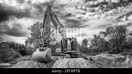 Escavatore cingolato durante i lavori di movimento terra in cantiere con vista banner in bianco e nero Foto Stock