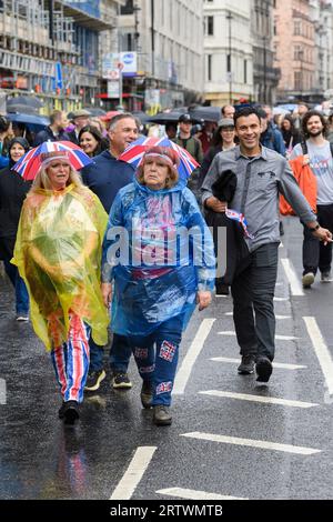 Due donne in costume Union Jack camminano lungo Piccadilly sotto la pioggia, parte di una grande folla di persone che sono venute a guardare l'incoronazione di re CH Foto Stock