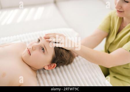 Vista ravvicinata dall'alto del bambino di cinque anni sottoposto a trattamento osteopatico o chiropratico in clinica pediatrica. Primo piano dell'osteopata che fa fisiologico Foto Stock