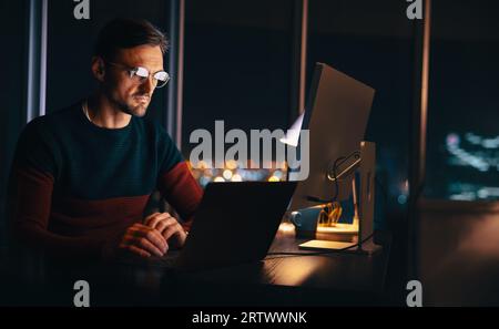 uomo d'affari che lavora fino a tardi nel suo ufficio domestico, partecipando a una riunione virtuale con il suo team. Uomo professionista che utilizza un laptop per comunicare e pianificare una pr Foto Stock