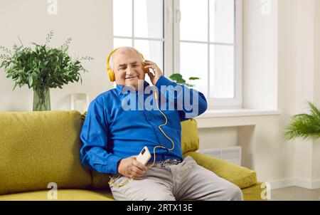 Uomo anziano sorridente in cuffia che ascolta podcast o musica tramite telefono Foto Stock
