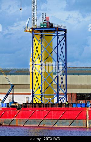 Produzione di nuove turbine eoliche giganti presso lo Smulders Howdon sul cantiere Tyne contro il cielo nuvoloso e blu che mostra la torre di supporto e il BOABARGE 66 Foto Stock