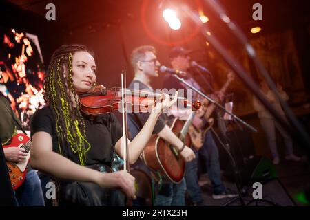 Una violinista femminile suona il violino. La band si esibisce sul palco, concerto di musica rock. Foto Stock