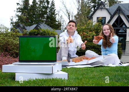 Giovane coppia adolescente in camicie bianche con picnic sul campo di girasole al tramonto. Mangiare pizza e bere champagne Foto Stock