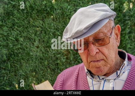 uomo maturo con cappello e occhiali che legge un libro fuori. Intrattenimento per anziani Foto Stock