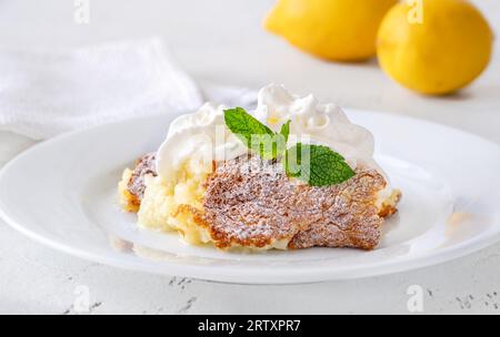 Porzione di budino di limone al forno guarnito con panna montata Foto Stock