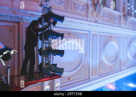 L'assistente del lavoratore di palcoscenico prepara le luci, l'ingegnere della luce, il tecnico dell'illuminazione che regola le luci per concerti e spettacoli musicali nella sala, l'installazione di una professione Foto Stock