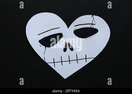 una carta halloween a forma di cuore con una faccia teschio su sfondo nero Foto Stock