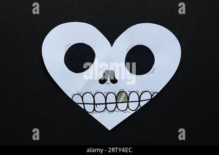 una carta halloween a forma di cuore con una faccia teschio su sfondo nero Foto Stock