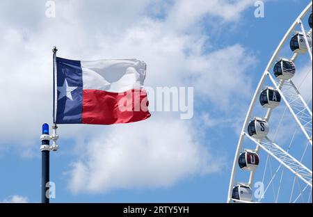 Bandiera dello stato del Texas che sventola su un cielo blu e su uno sfondo bianco. Vista parziale di una ruota panoramica inclusa. Foto Stock