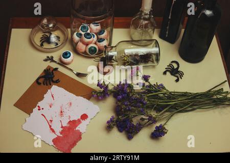 natura morta di halloween con una carta bianca e sanguinosa, palline oculari, scorpioni, insetti e fiori secchi Foto Stock