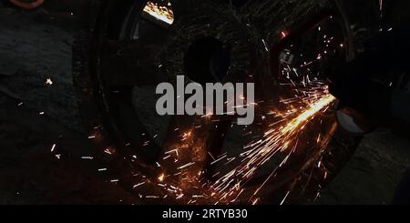 Fabbro in abiti speciali e occhiali di protezione lavori in produzione. Lavorazione del metallo con smerigliatrice angolare. Scintille nella lavorazione dei metalli Foto Stock