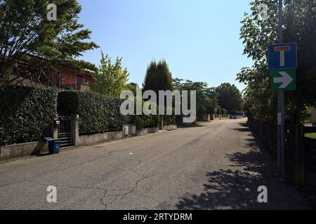 Strada delimitata da recinzioni e piante di giardini appesi fuori dalle mura di un villaggio italiano in una giornata di sole Foto Stock