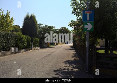 Strada delimitata da recinzioni e piante di giardini appesi fuori dalle mura di un villaggio italiano in una giornata di sole Foto Stock